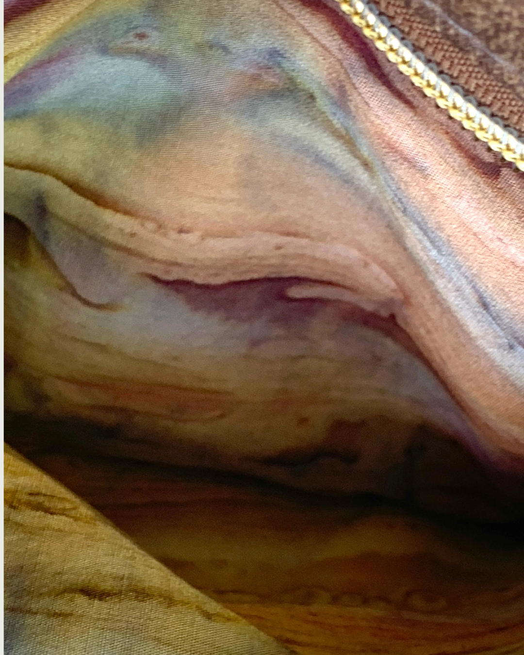 Handmade crossbody bag closeup view of an open zippered pocket showing the pocket lining of an autumn watercolored striped cotton woven fabric.