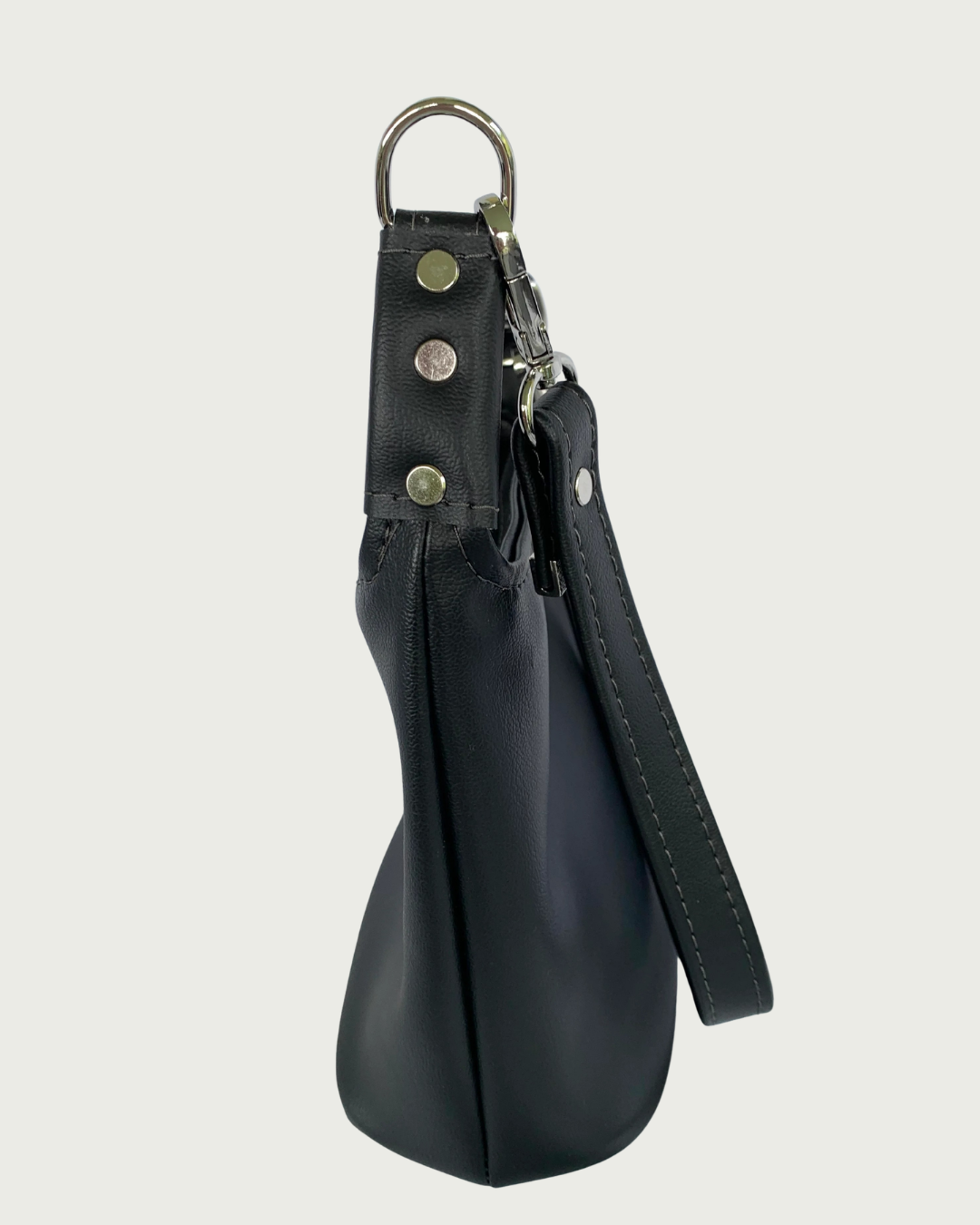 Handcrafted black vinyl slouchy shoulder bag side view with detachable strap and nickel hardware including studs or rivets on the strap connectors.
