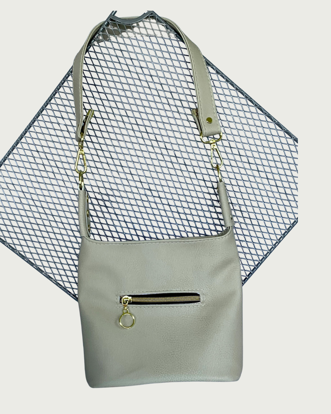 A solid beige vinyl shoulder bag with small exterior zippered pocket showing the length of the strap.