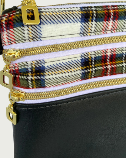 Closeup view of handmade crossbody bag of black faux leather and red, black and white classic plaid cotton flannel. Two zippered pockets have gold-tone open square pulls, gold-tone zipper teeth, and white zipper tape. The open square pull from the top zippered closure is showing.