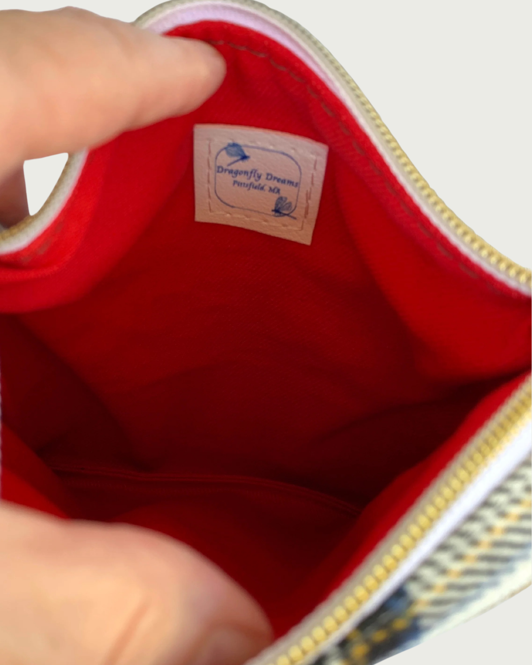 Interior view of Handmade crossbody bag of classic red, black, and white cotton plaid fabric revealing a red, pink, and white floral printed cotton lining with a sewn-in Dragonfly Dreams label. The top zippered closure has gold-tone zipper teeth and white zipper tape.