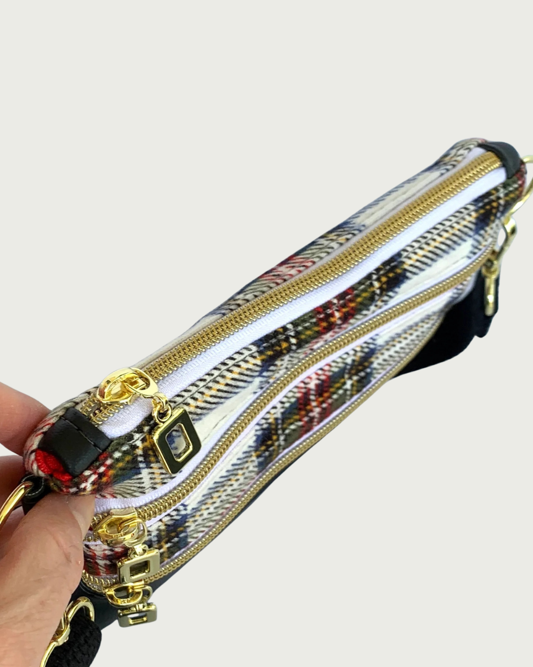 Top view of Handmade crossbody bag of red, black, and white plaid with black faux leather accents. The top zippered closure and the two zippered pockets have gold-tone open square pulls, gold-tone zipper teeth, and white zipper tape.