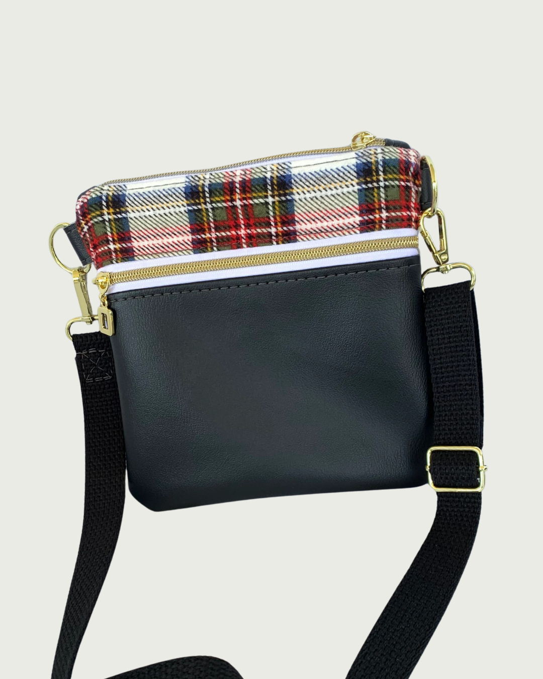 Handcrafted crossbody bag of classic red, black, and white plaid with black faux leather accents, gold-tone zipper details on top closure and pocket, and a black adjustable. detachable cotton webbing shoulder strap, shown on a light gray background.