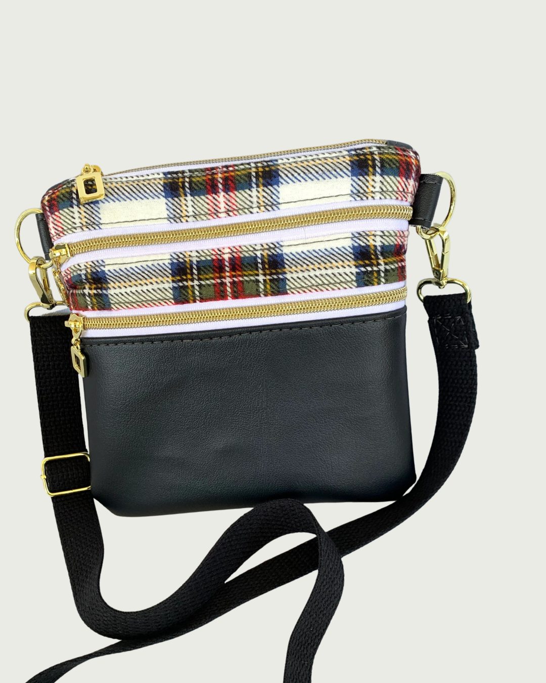 Handcrafted crossbody bag of classic red, black, and white plaid with black faux leather accents, gold-tone zipper details on top closure and 2 pockets, and a black adjustable. detachable cotton webbing shoulder strap, shown on a light gray background.