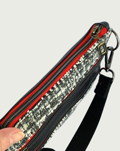 Top view of Handmade crossbody bag of black and white tweed with black faux leather accents. The top zippered closure and the two zippered pockets have gunmetal open square pulls, gunmetal zipper teeth, and red zipper tape.