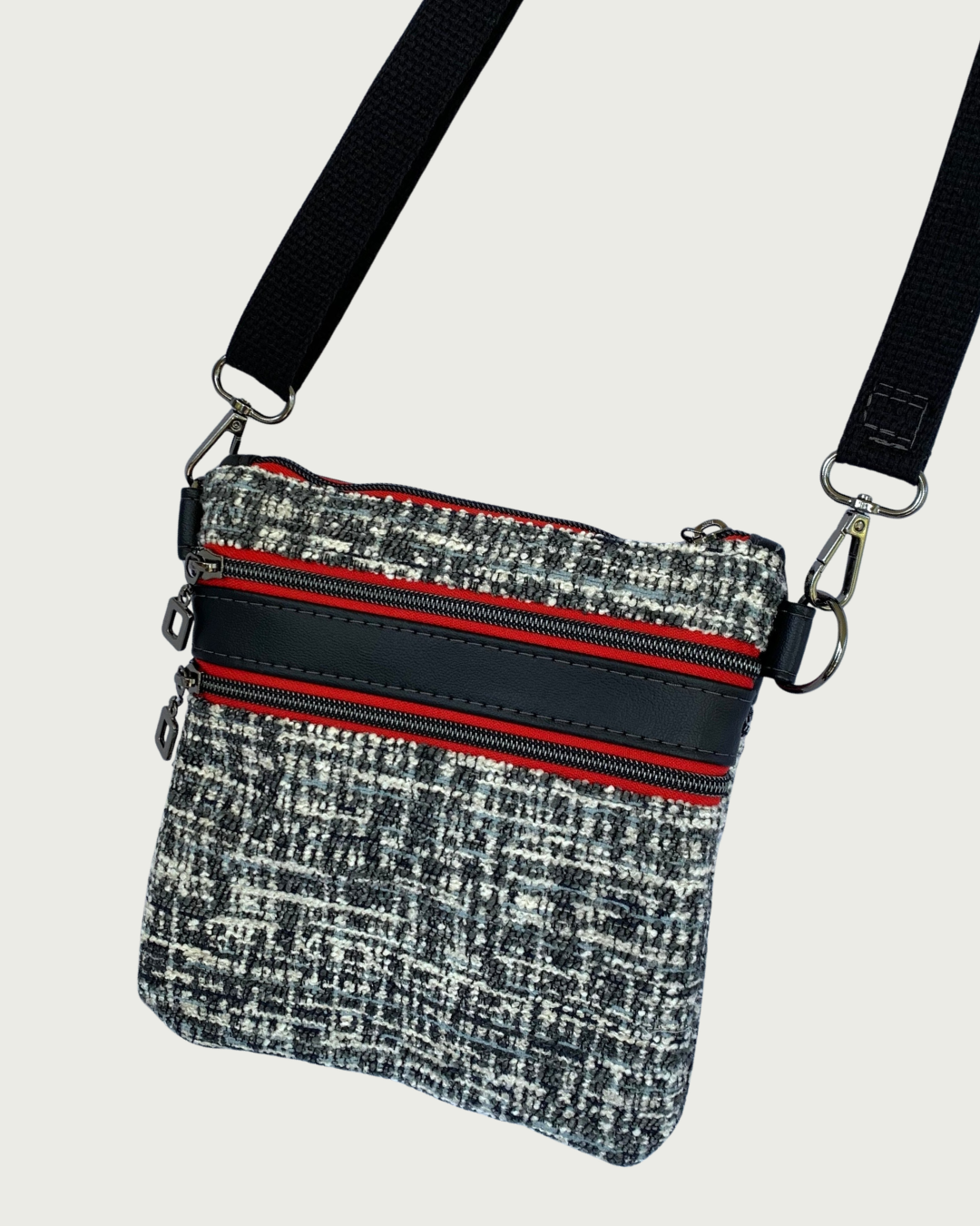 Handcrafted crossbody bag of black and white tweed with black faux leather accents, gunmetal zipper details on red zipper tape of top closure and 2 pockets, and a black adjustable. detachable cotton webbing shoulder strap, shown on a light gray background.