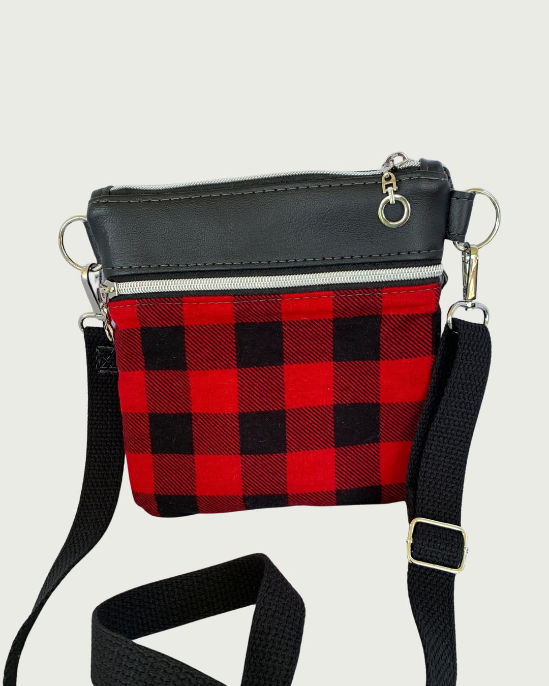 Handcrafted red and black buffalo plaid crossbody bag with black faux-leather accents, nickel zipper details, and a black adjustable. detachable cotton webbing shoulder strap, shown on a light gray background.