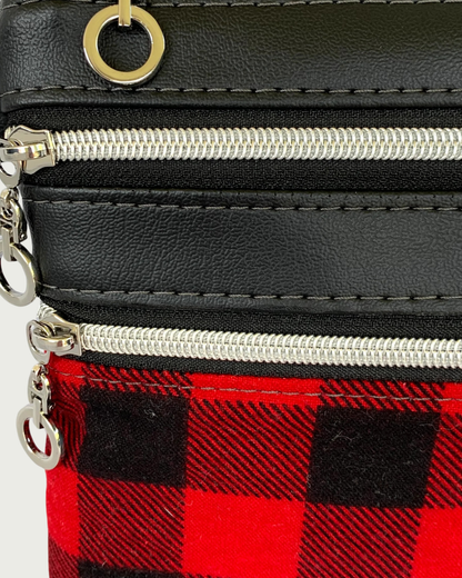 Closeup view of handmade crassbody bag of black faux leather and red and black buffalo plaid cotton flannel. Two zippered pockets have nickel dangle circle pulls, nickel-colored zipper teeth, and black zipper tape. The circle pull from the top zippered closure is showing.