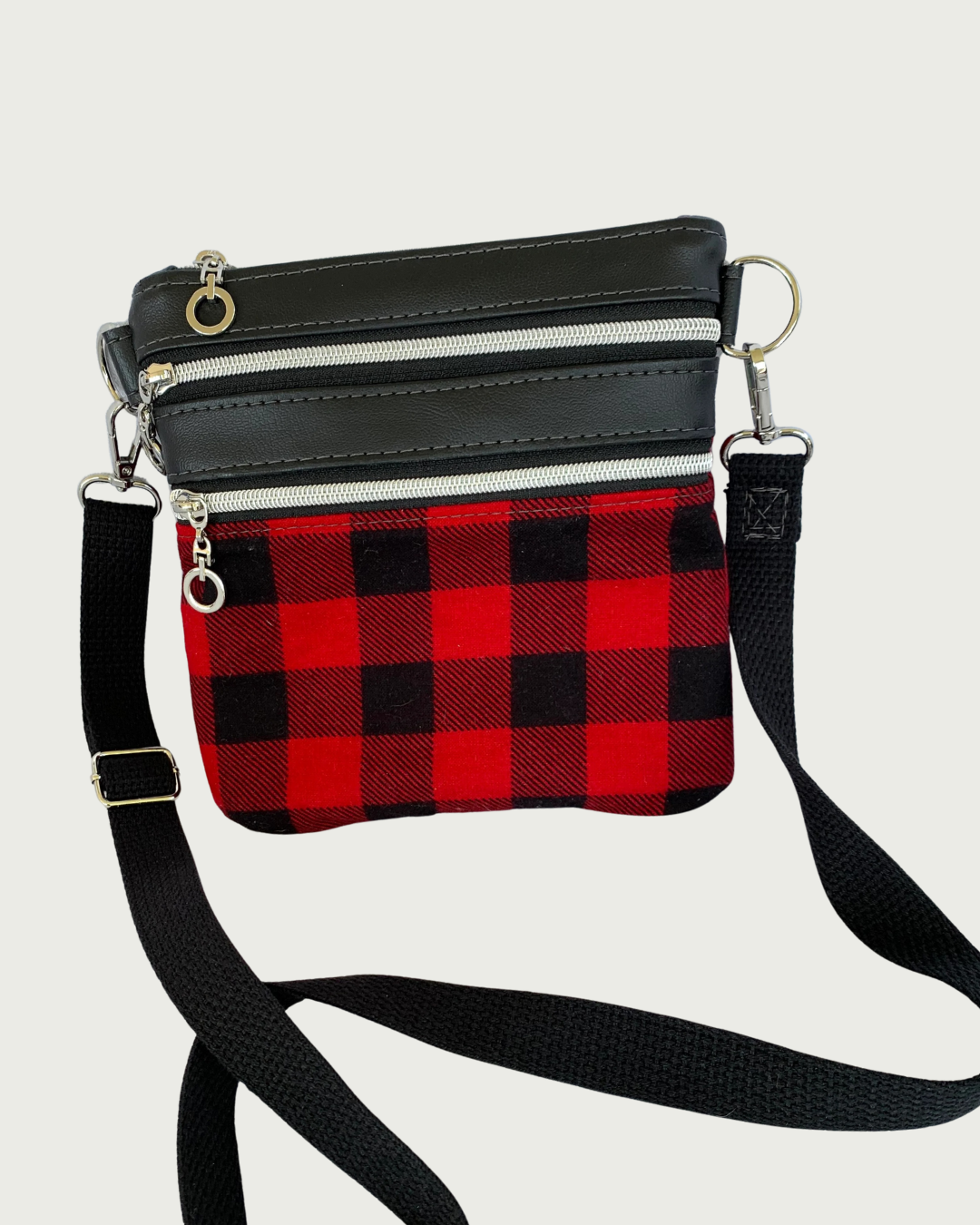 Handcrafted red and black buffalo plaid crossbody bag with black faux-leather accents, nickel zipper details, and a black adjustable. detachable cotton webbing shoulder strap, shown on a light gray background.