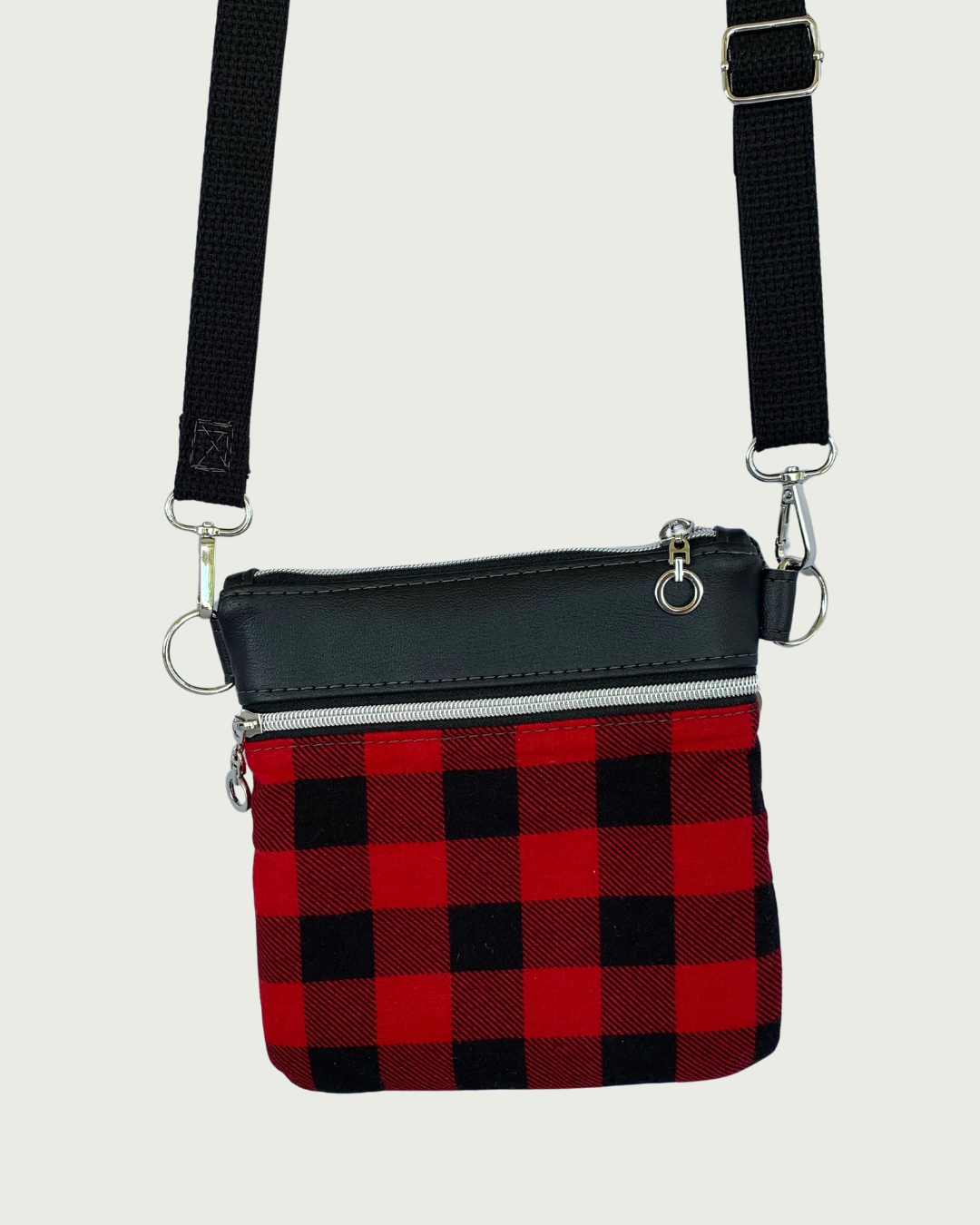 Handcrafted red and black buffalo plaid crossbody bag with black faux-leather accents, nickel zipper closure and pocket details, and a black adjustable. detachable cotton webbing shoulder strap, shown on a light gray background.