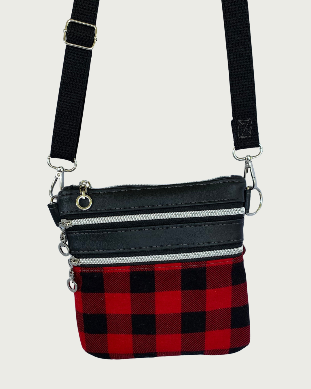 Handcrafted red and black buffalo plaid crossbody bag with black faux-leather accents, nickel zipper details on closure and 2 pockets, and a black adjustable. detachable cotton webbing shoulder strap, shown on a light gray background.