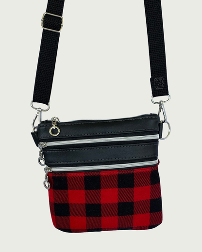Handcrafted red and black buffalo plaid crossbody bag with black faux-leather accents, nickel zipper details on closure and 2 pockets, and a black adjustable. detachable cotton webbing shoulder strap, shown on a light gray background.