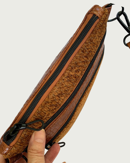 Handmade crossbody bag of brown chenille fabric with brown textured faux leather accents including an adjustable and detachable shoulder strap as viewd from the top. Matt black hardware throughout such as on the two zippered pockets and the top zippered closure with rope zipper pulls.