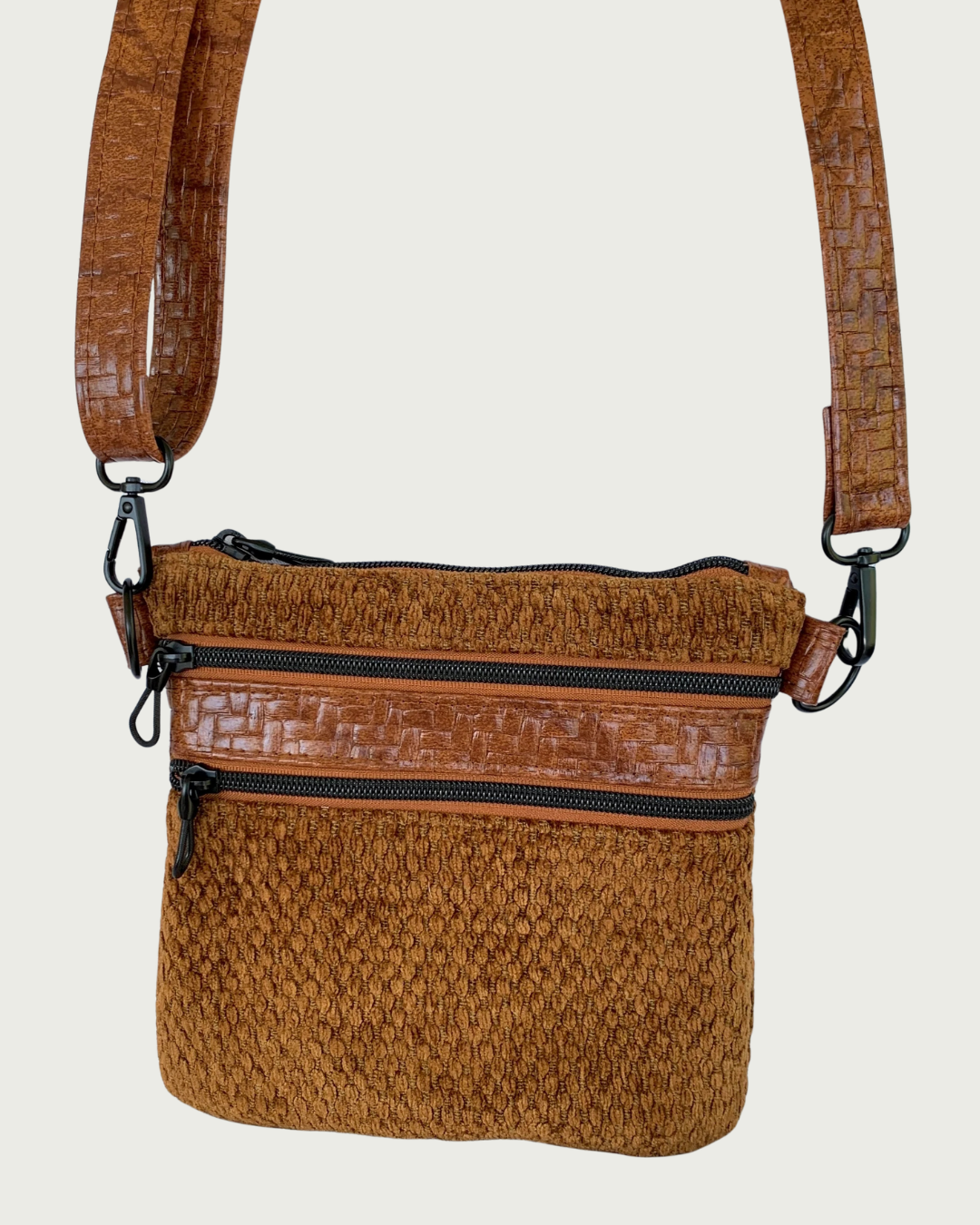 Handmade crossbody bag of brown chenille fabric with brown textured faux leather accents including an adjustable and detachable shoulder strap. Matt black hardware throughout as is on the two zippered pockets and the top zippered closure with rope zipper pulls.
