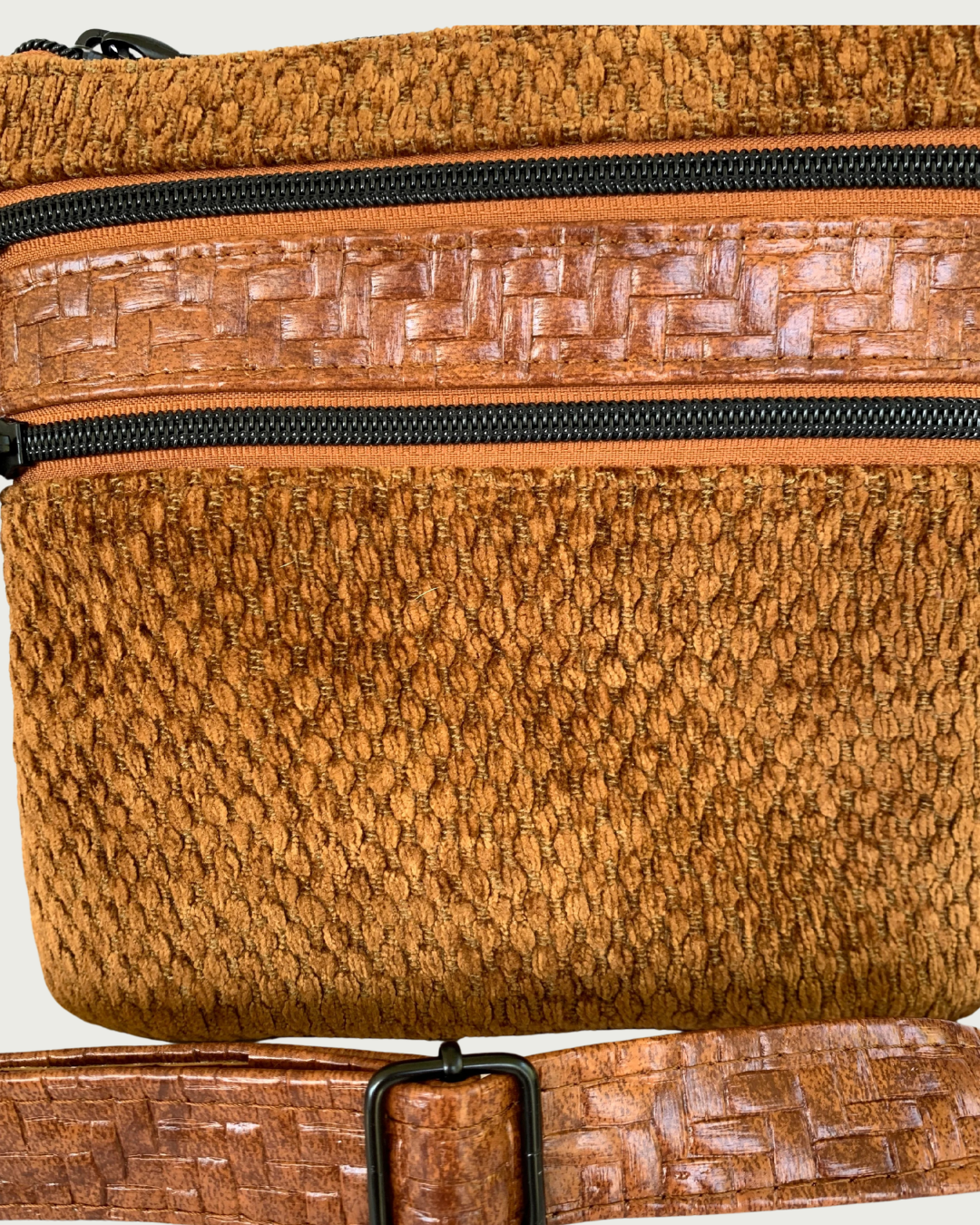 Handcrafted crossbody bag of brown chenille fabric with brown textured faux leather accents including an adjustable and detachable shoulder strap. Matt black hardware on the zipper teeth and the zipper pulls on the two cinnamon colored zippered pockets.