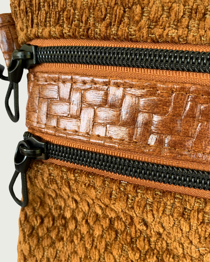 A detailed closeup view of a two zippers on a handcrafted crossbody bag of brown chenille fabric with brown textured faux leather accents. The zipper tape is a cinnamon color, and the zipper teeth and pulls that are shaped like ropes are of a matt black color.