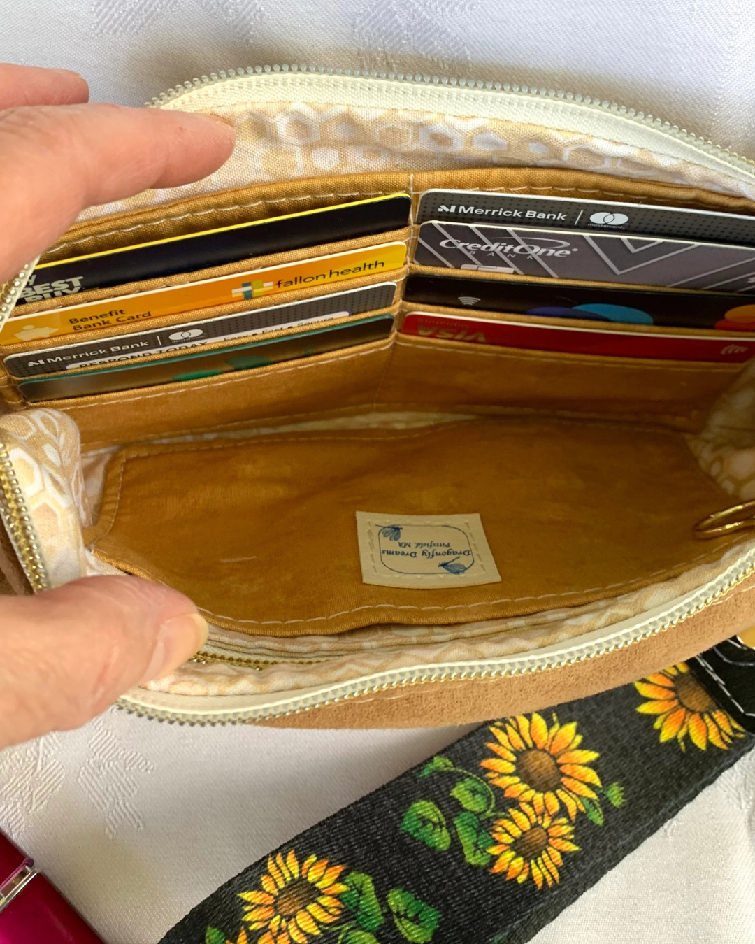 Handmade wristlet wallet interior showing 8 full card slots and 2 slip pockets. A wide back woven strap with sunflowers lies next to it.