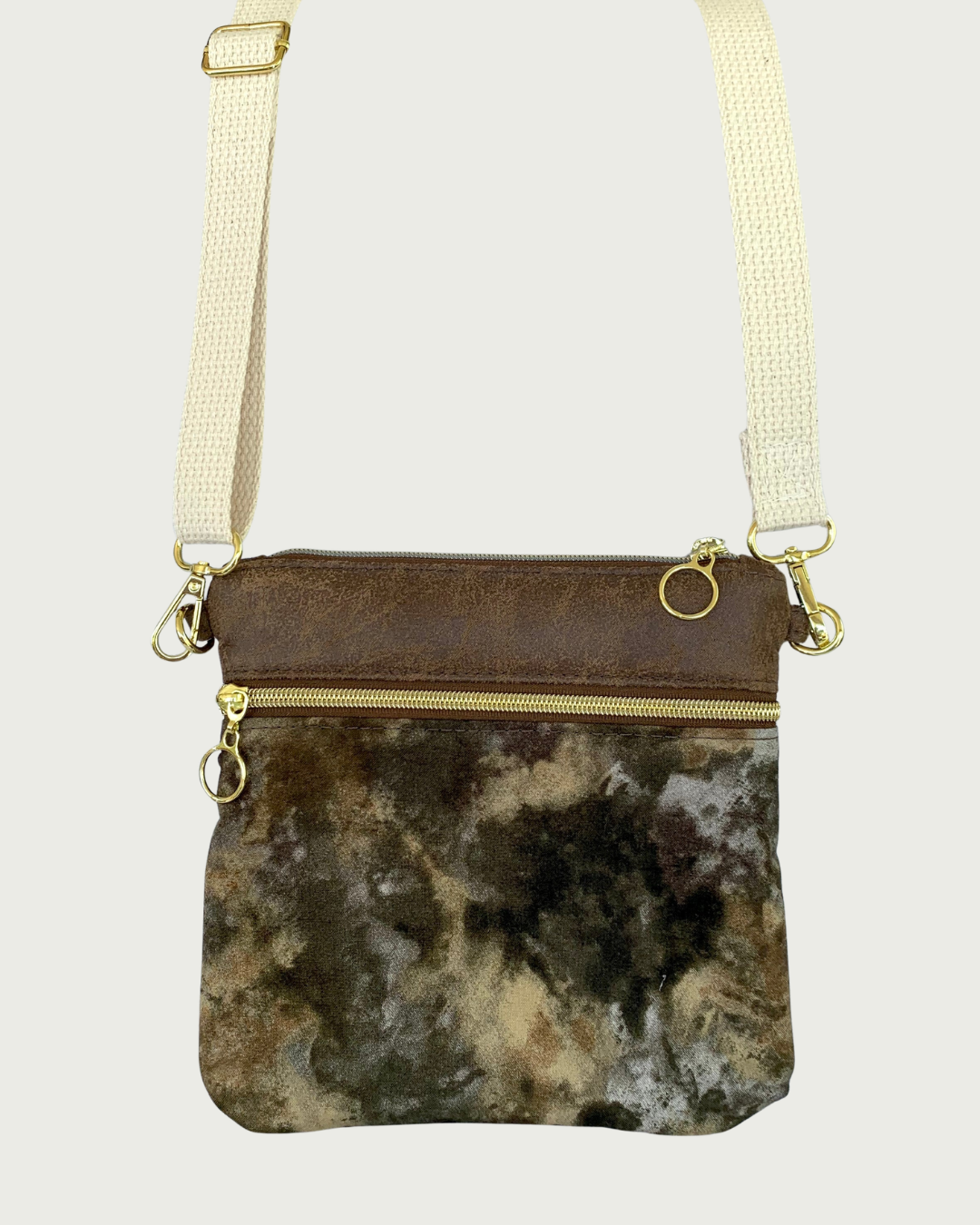 Handmade crossbody bag with camouflage print body and brown, distessed leather accents, a zippered pocket and a top zippered closure with cirlcle zipper pulls, a natural colored cotton webbing adjustable and detachable shoulder strap, and gold-tone hardware throughout.