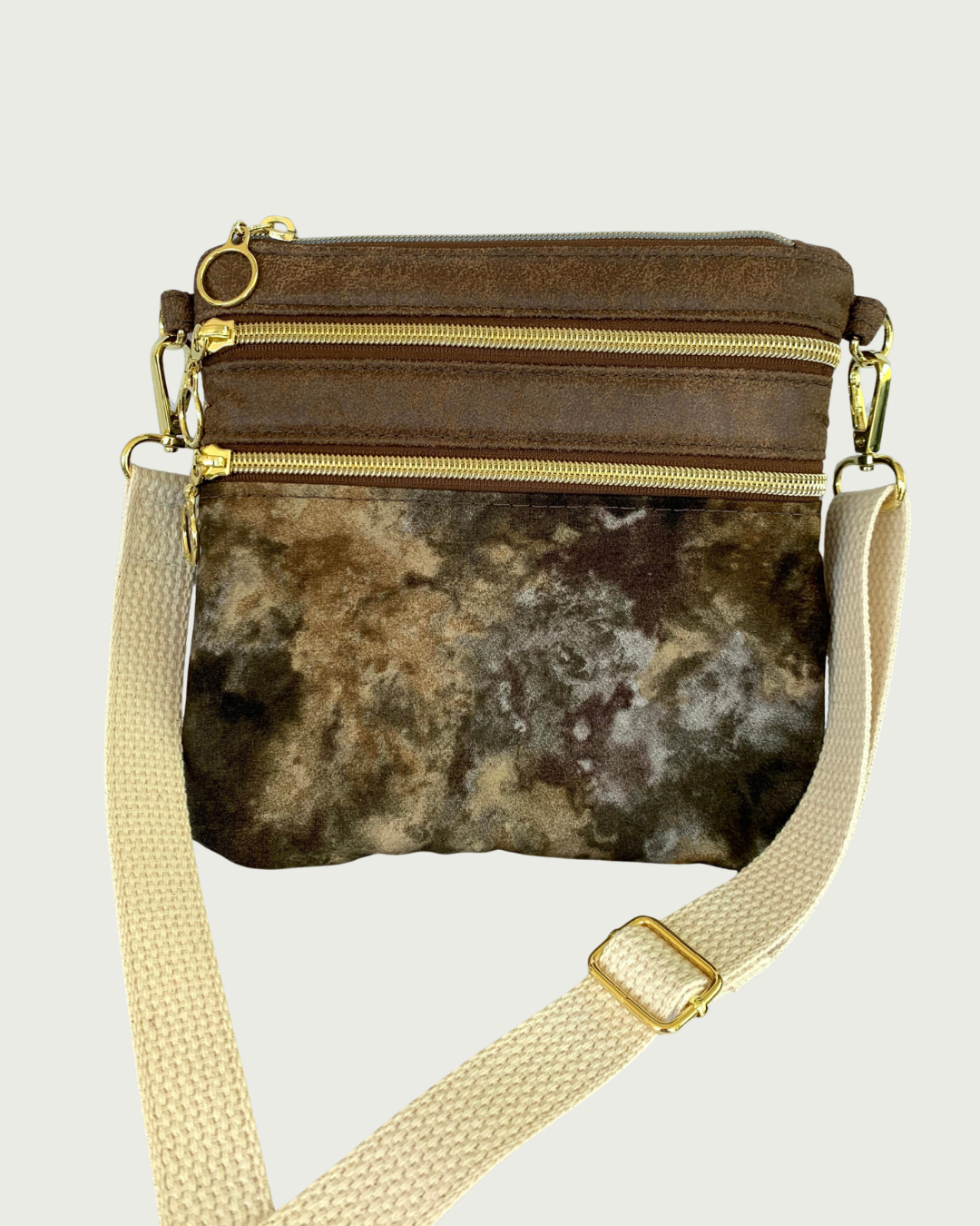 Handcrafted crossbody bag with camo print body and brown, distessed leather accents, two zippered pockets and a top zippered closure with cirlcle zipper pulls, a natural colored cotton webbing adjustable and detachable shoulder strap, and gold-tone hardware throughout.