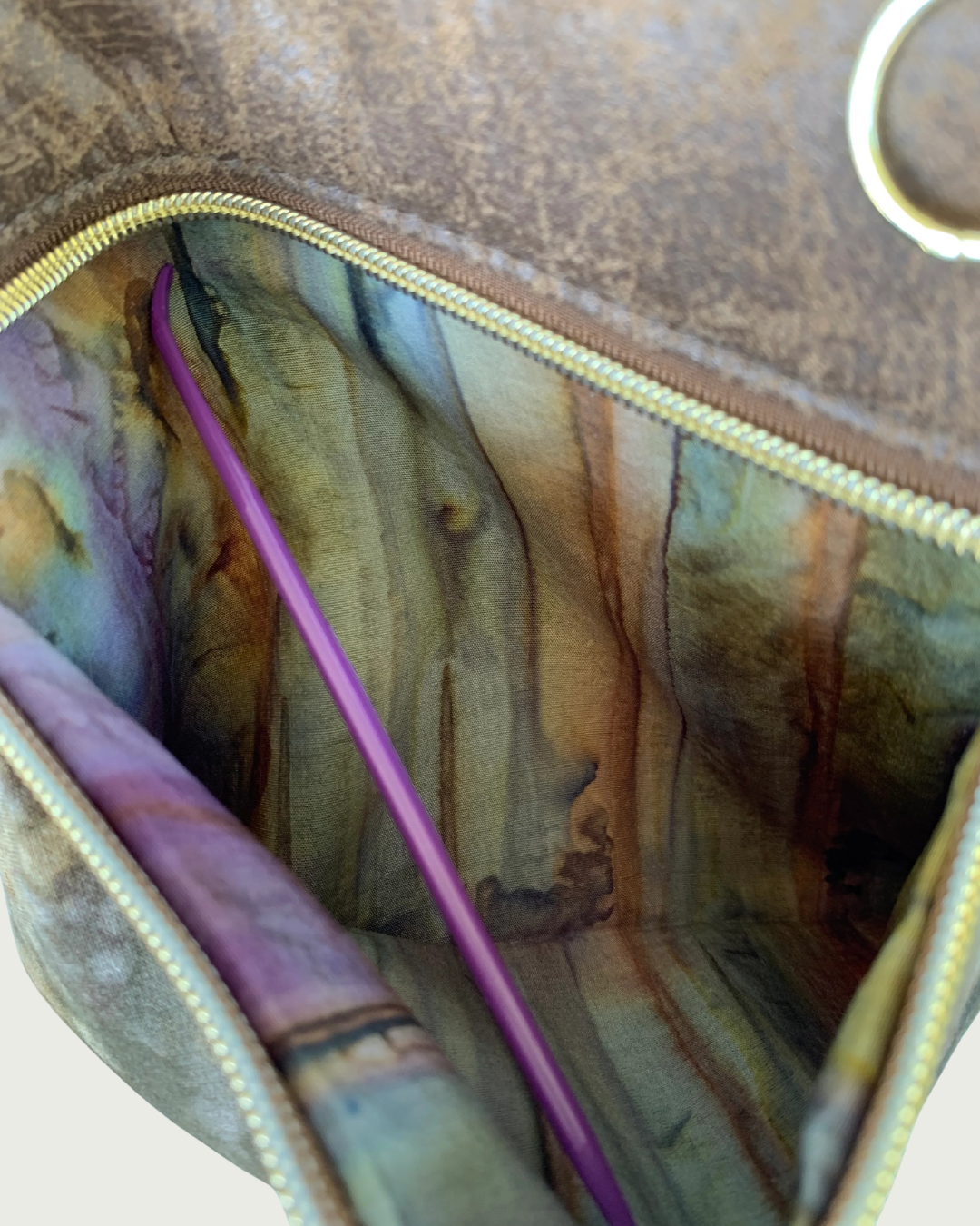 Handcrafted crossbody bag with camo print body and brown, distessed leather accent closeup view of an open zippered pocket showing the pocket lining of an autumn watercolored striped cotton woven fabric