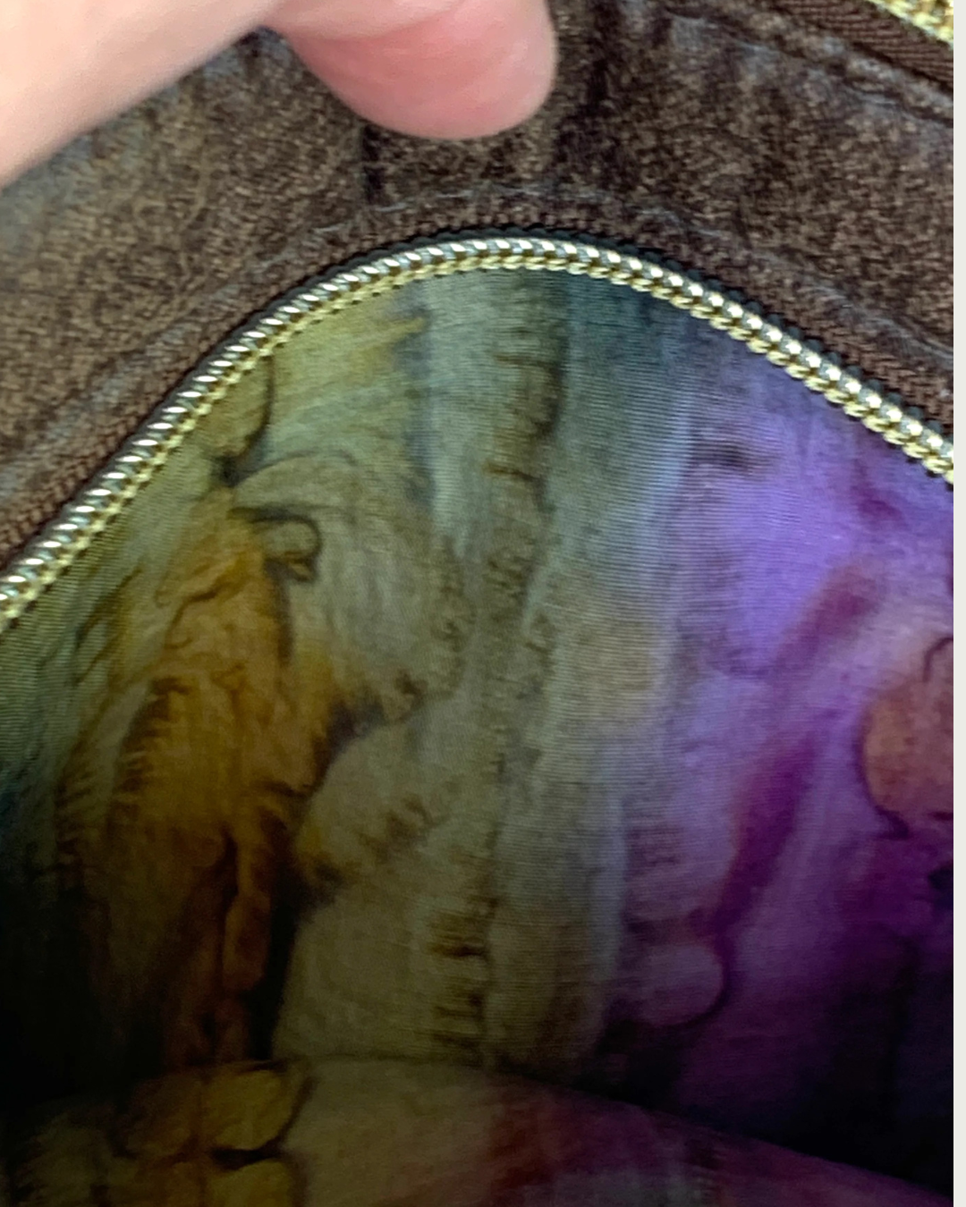Handmade crossbody bag closeup view of an open zippered pocket showing the pocket lining of an autumn watercolored striped cotton woven fabric.