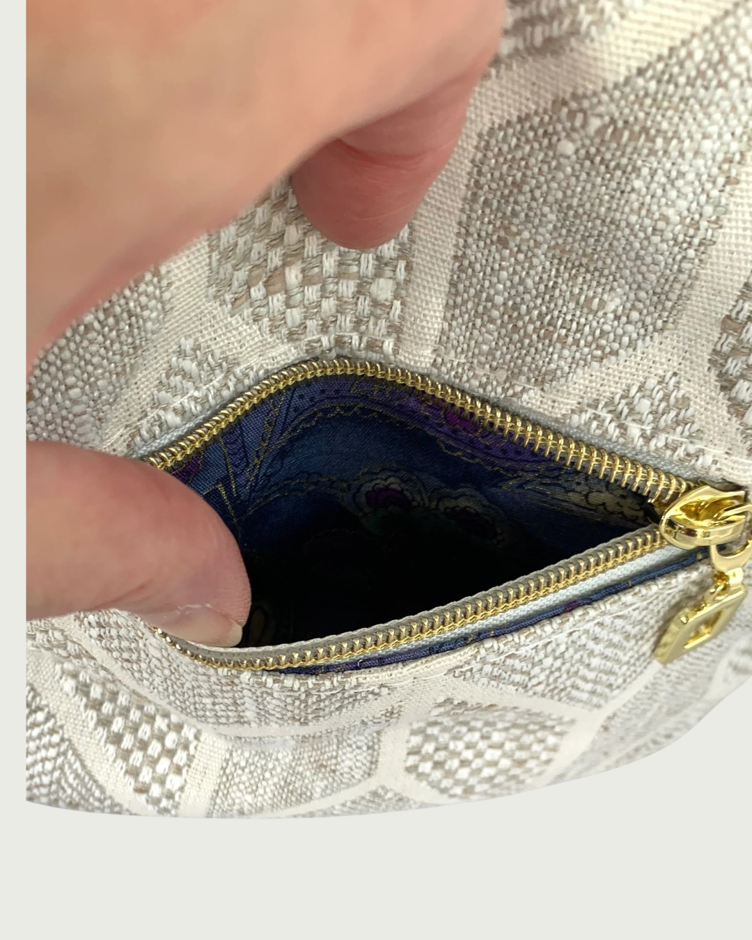 A handcrafted neutral colored shoulder bag . Closeup view of small zippered external pocket.