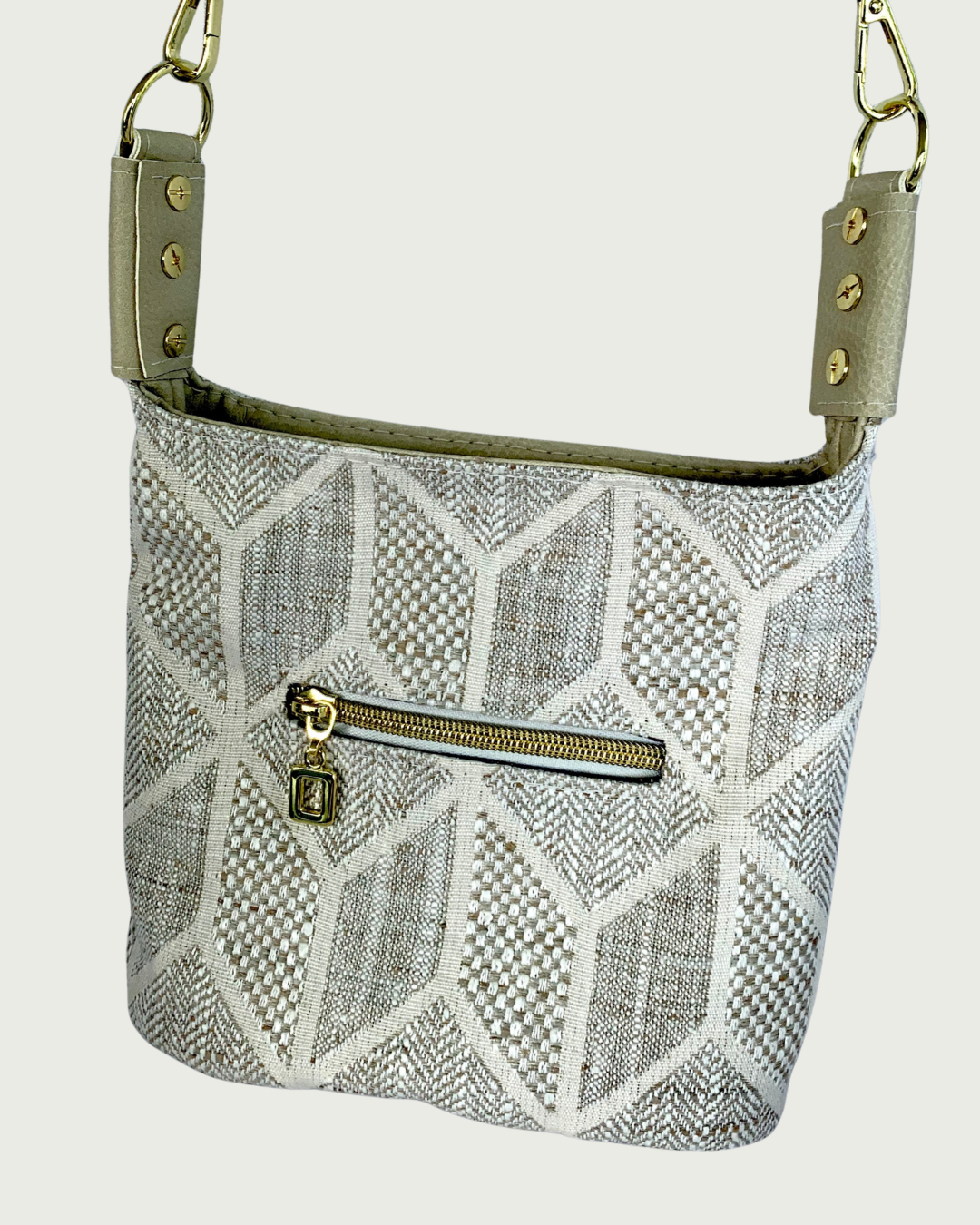 Closeup view of a handcrafted chevron slouchy shoulder bag in neutral colors with beige vinyl strap and trim. Small external zipper pocket.