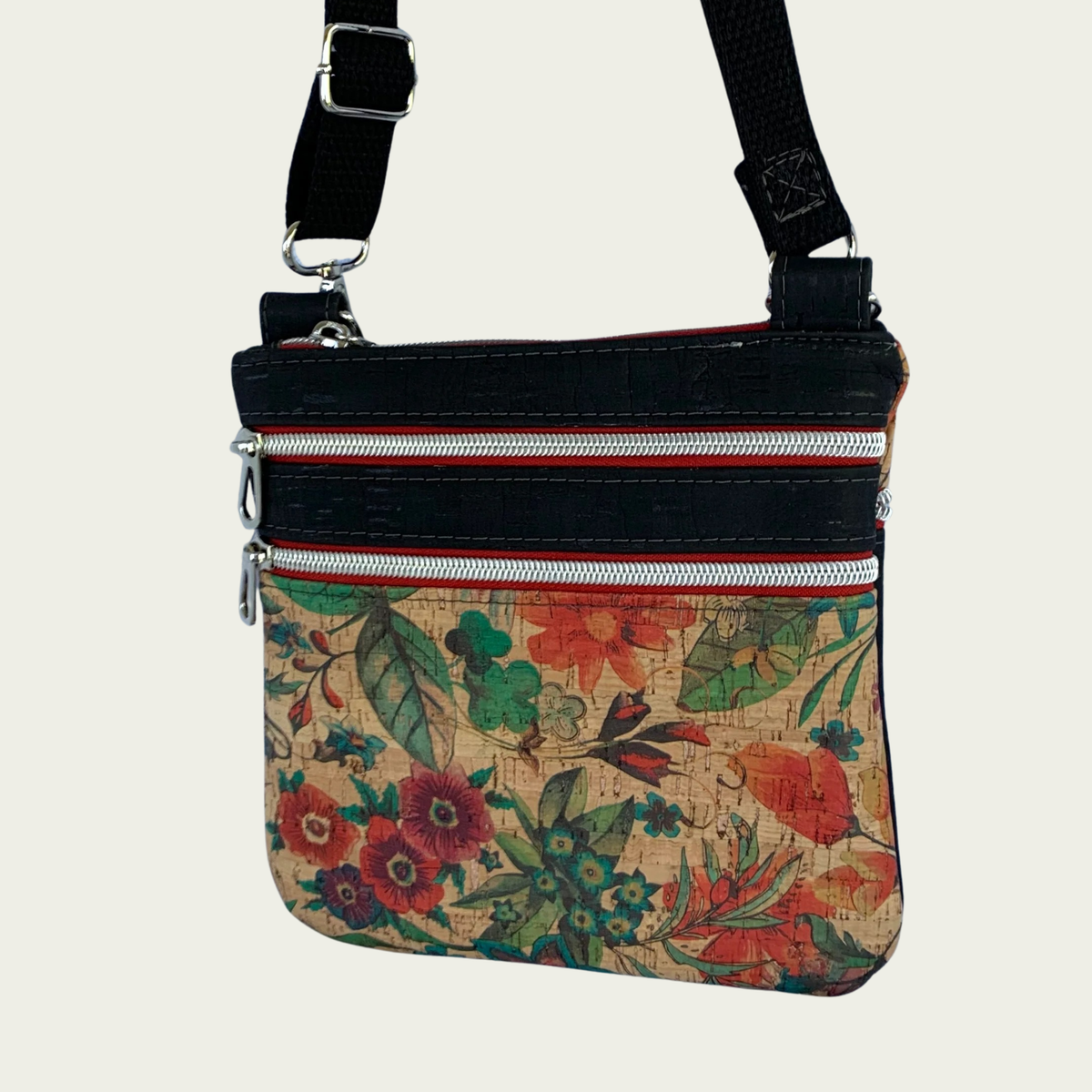 Floral patterned cork crossbody bag with black cork accents and a black cotton webbing strap and multiple zippered pockets inaddition to top zipper closure.
