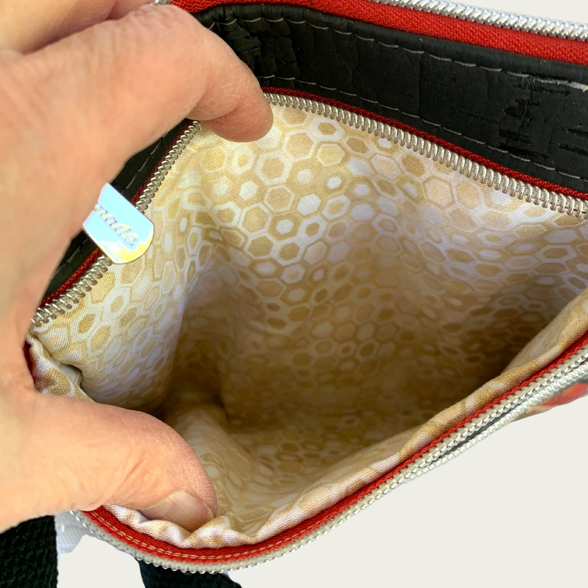 View of the inside of a pocket of a cork handbag. The lining is a geometric pattern in gold, white, and tan.