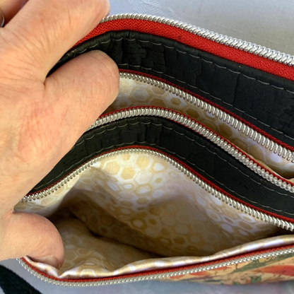 A closeup view of a cork handbag with 3 zippers. A hand is holding two of the zippers to pockets. The other zipper is closed on top of the bag. The pocket linings are a small geometric print in tan, gold, and white.