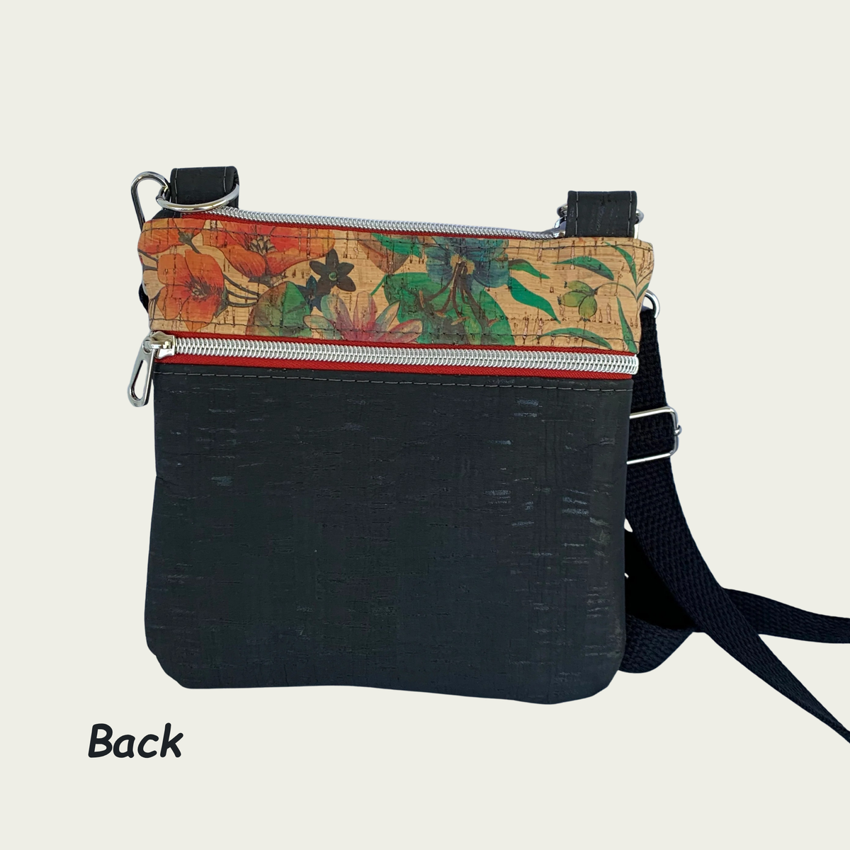 Back view of  a solid black rustic cork crossbody bag with floral cork accents, black cotton webbing strap, nickel hardware, and a zipperd pocket.