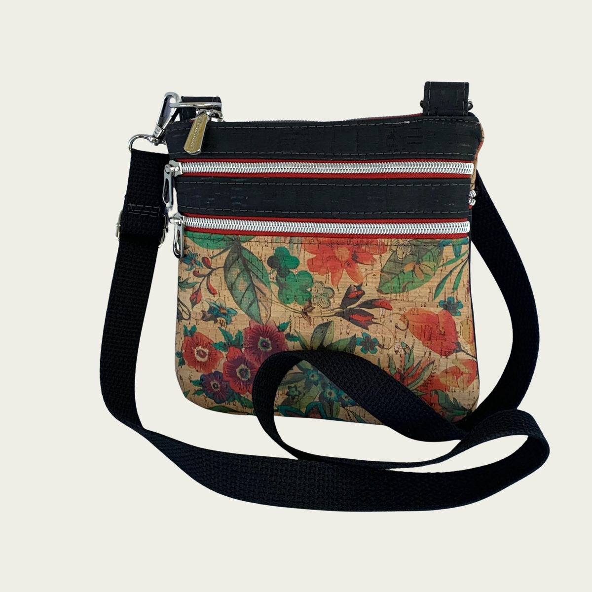 Floral patterned cork crossbody bag with black cork accents and a black cotton webbing strap and multiple zippered pockets inaddition to top zipper closure.