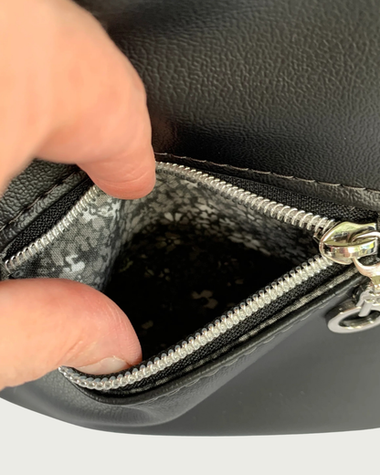 Handcrafted black vinyl slouchy shoulder bag with closeup view of a small exterior zippered pocket. The lining is a black and gray calico.