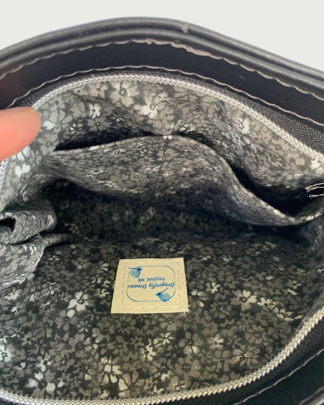 Handcrafted black vinyl shoulder bag with closeup view of the interior with slip pockets. The lining is a black and gray calico and there is a label for Dragonfly Dreams sewn in.