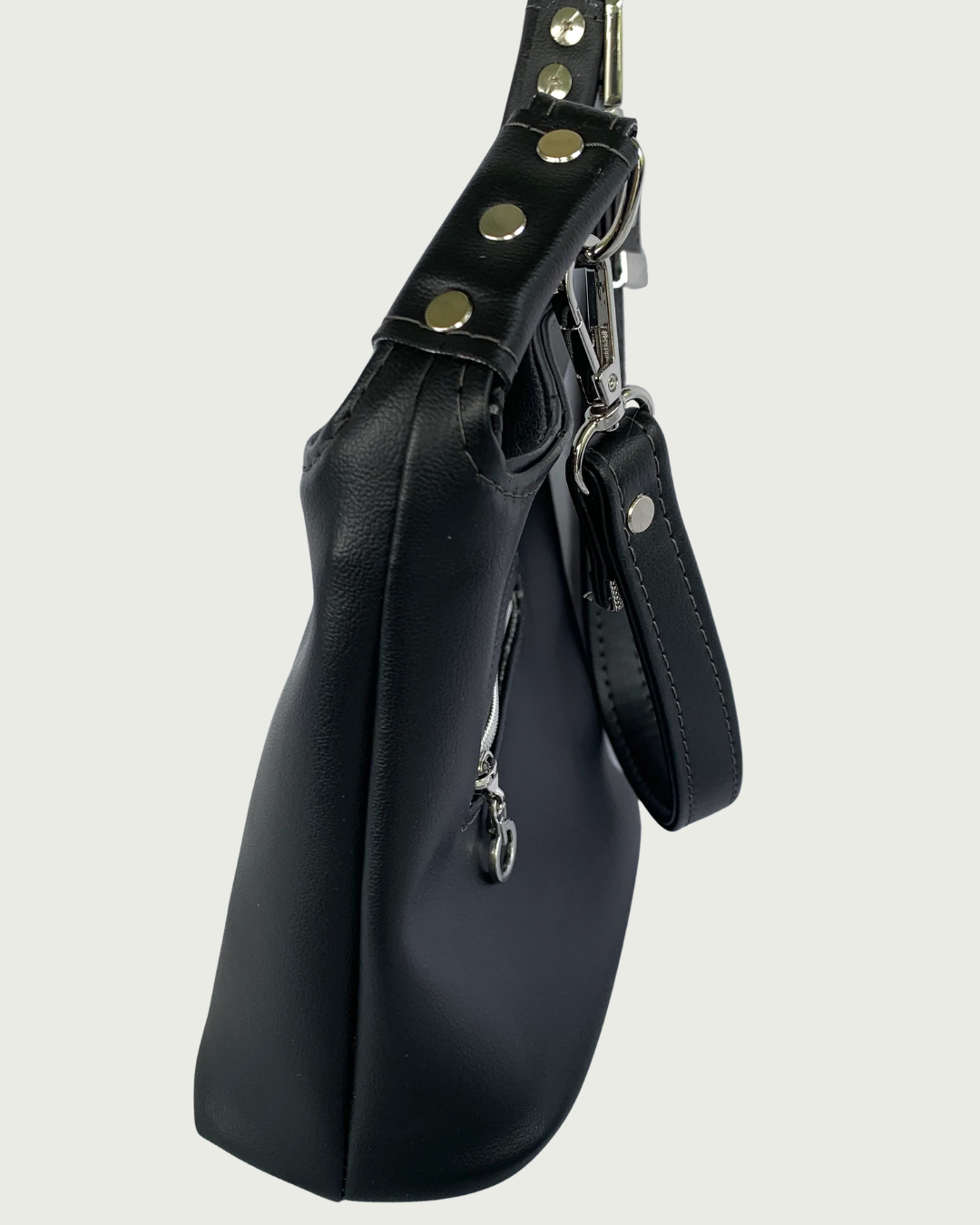 Handcrafted black vinyl slouchy shoulder bag side view with detachable strap and nickel hardware including studs or rivets on the strap connectors.