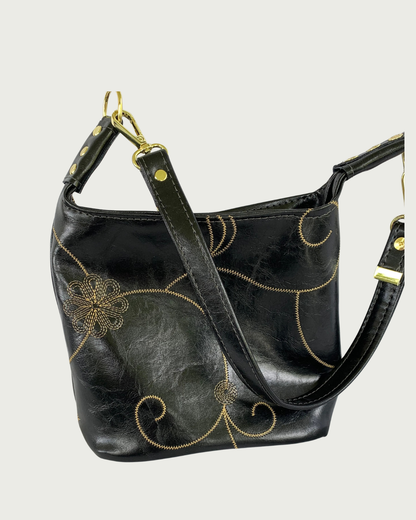 Handcrafted black vinyl slouchy shoulder bag with decorative gold stitching, gold hardware, and detachable strap.
