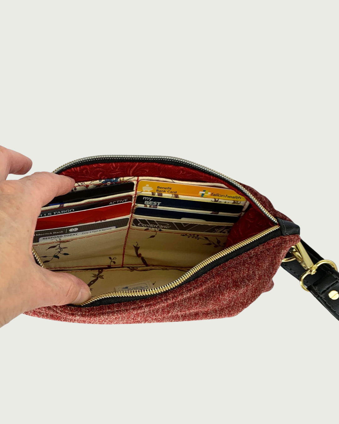A hand holding open a handmade merlot chenille-like polyester wristlet wallet revealing eight built-in card slots filled with cards and a slip pocket behind it.