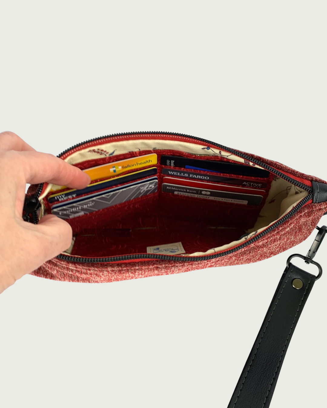 Handcrafted merlot chenille-like polyester wristlet wallet featuring matt black hardware. A hand holds open the top zipper revealing color-coordinated lining with a built-in card slot filled with 8 cards.