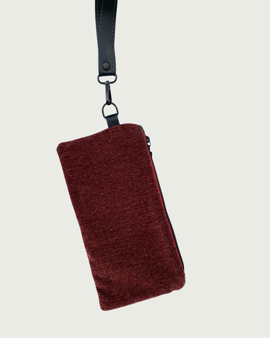 Handcrafted merlot chenille-like polyester wristlet wallet hanging by a detachable, black faux leather wrist strap. Matt black hardware including an open square top zipper of burgundy zipper tape.