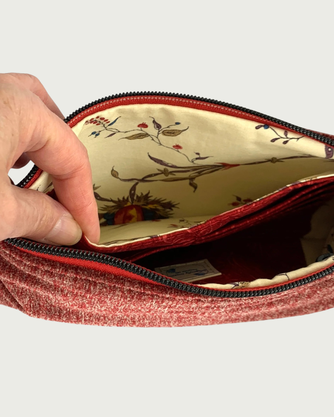 Handcrafted merlot chenille-like polyester wristlet wallet featuring matt black zipper on burgundy zipper tape held open by a hand showing a spacious slip pocket behind a card slot panel.