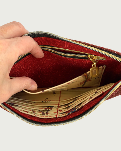 Handcrafted merlot chenille-like polyester wristlet wallet held open by a hand revealing a slip pocket and zippered pocket with a Dragonfly Dreams label sewn in. The pocket and main zipper teeth and open square pull are gold-tone and are on a black zipper tape. Eight buit-in card slots can be seen on the other side of the bag’s interior.