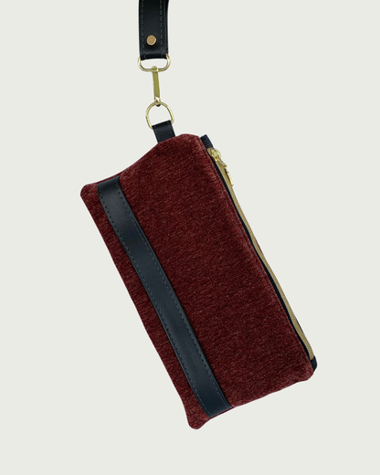 Handcrafted merlot chenille-like polyester wristlet wallet featuring black faux leather accents including a detachable wrist strap. The hardware is gold-tone such as on an open square pull and zipper teeth on black zipper tape.
