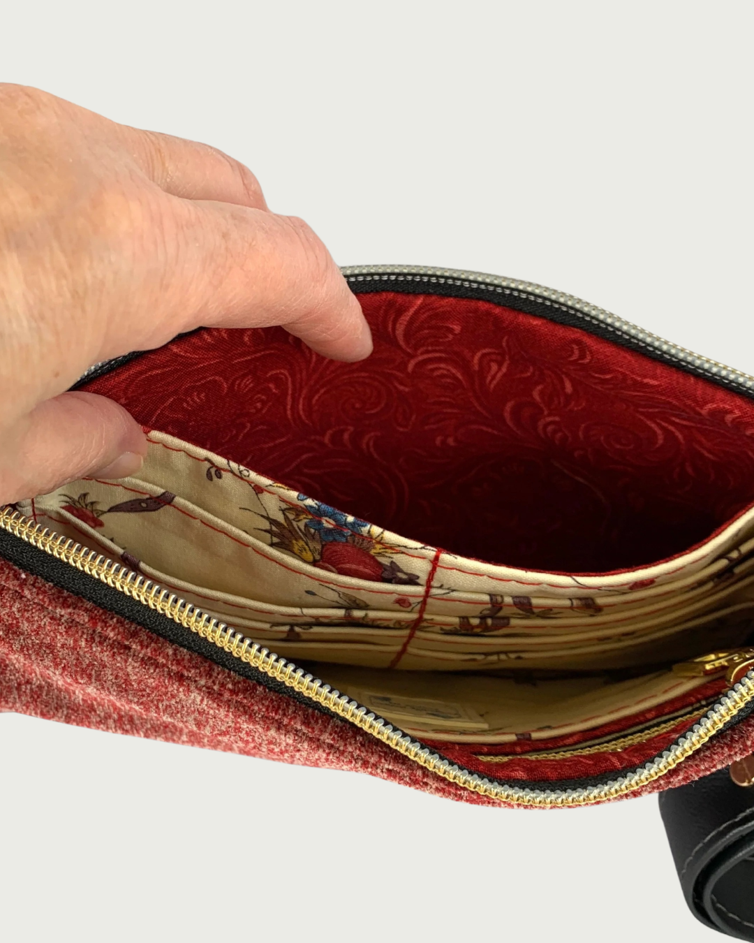 Handcrafted merlot chenille-like polyester wristlet wallet featuring gold-tone zipper on black zipper tape held open by a hand showing a spacious slip pocket behind an eight card-slot panel.