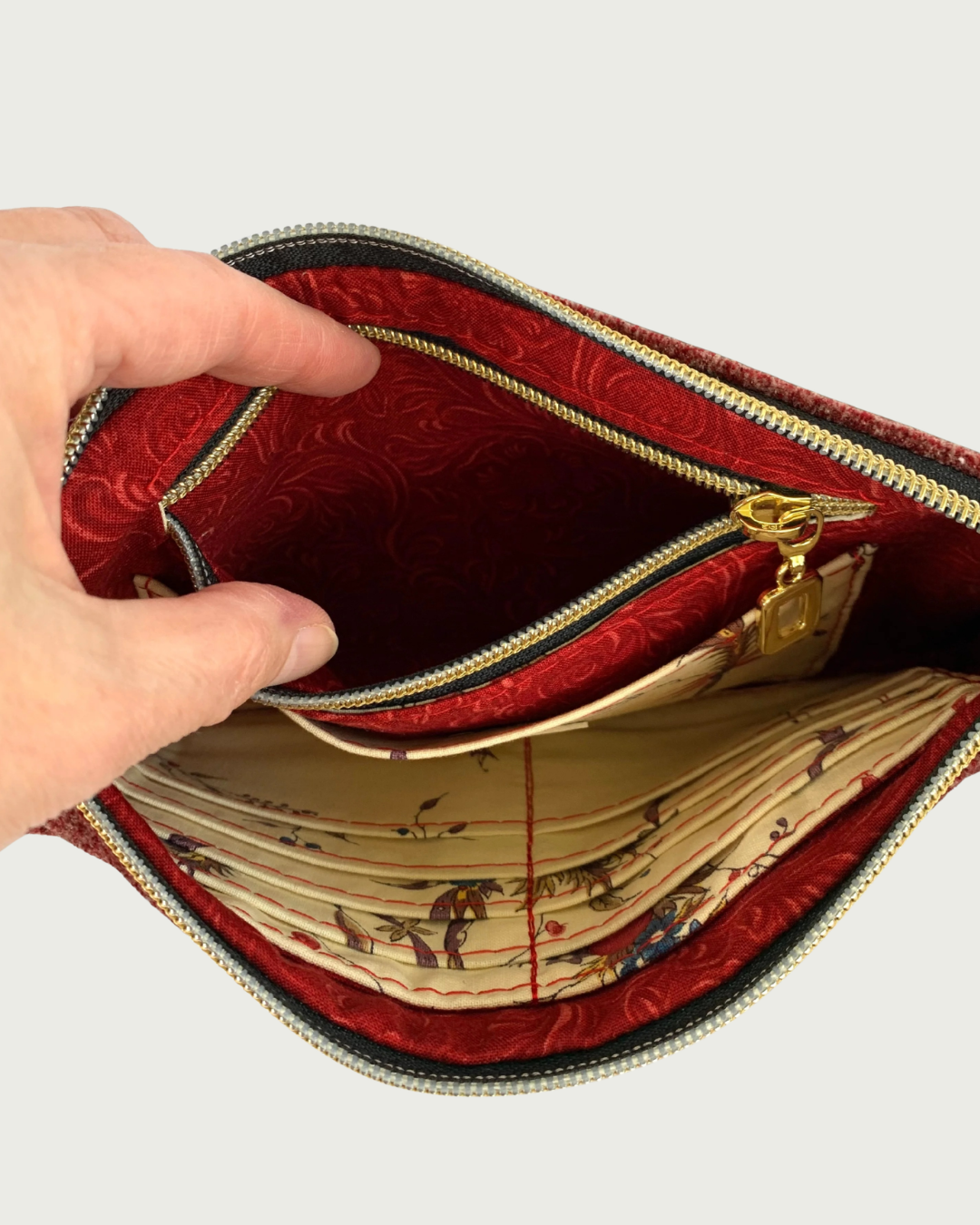Handcrafted merlot chenille-like polyester wristlet wallet featuring gold-tone hardware. A hand holds open the bag open revealing color-coordinated lining and an open zipper pocket with a slip pocket in front of it. On the opposite side, you can see a built-in card slot filled with 8 .