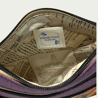 The interior of a purple cork handbag. The lining is images of aged pages of classic books. Three zippers are shown.