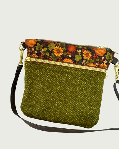 Handmade olive green crossbody bag with a textured fabric body, a zippered pocket featuring a pumpkin and sunflower patterned band above it, gold-tone hardware, a top zippered closure, and a thin, coffe adjustable and detachable shoulder strap.