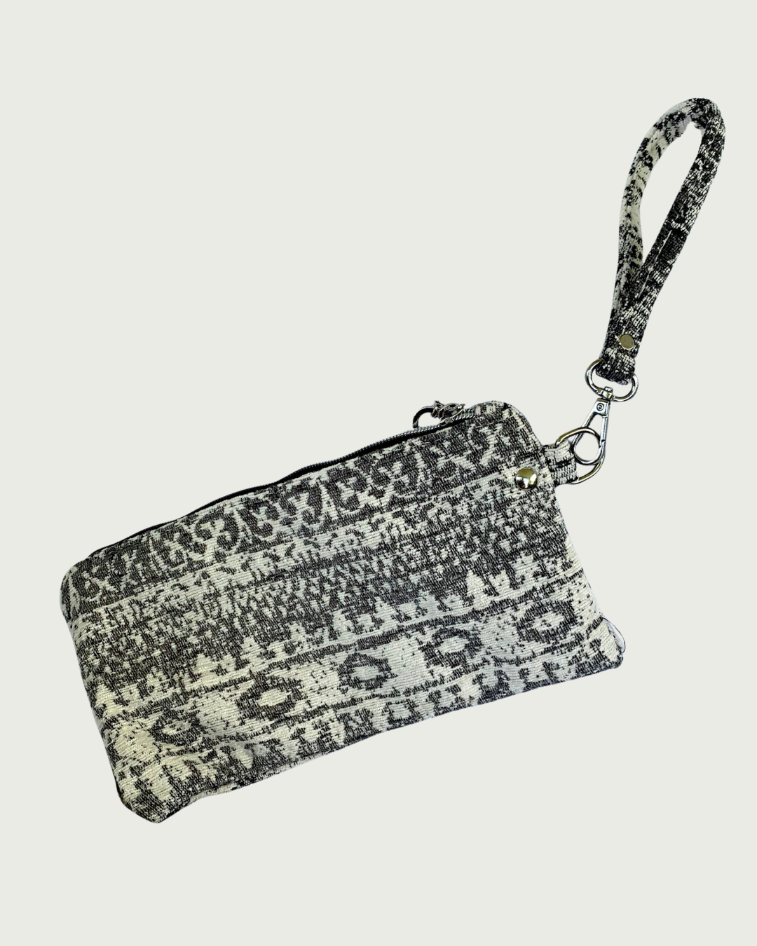 A wristlet in a gray and ivory fair isle-like print with a top zipper closure, gunmetal hardware, and and detachable wrist strap.