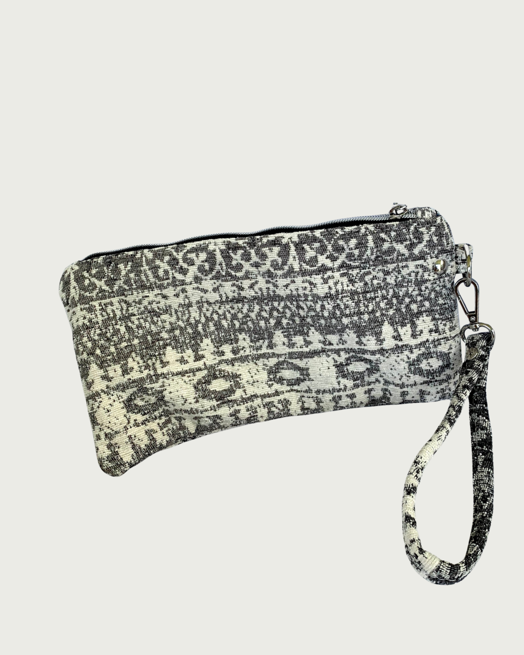 A wristlet in a gray and ivory fair isle-like print with a top zipper closure, gunmetal hardware, and and detachable wrist strap.