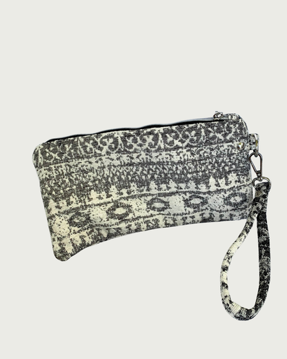A wristlet in a gray and ivory fair isle-like print with a top zipper closure, gunmetal hardware, and and detachable wrist strap.