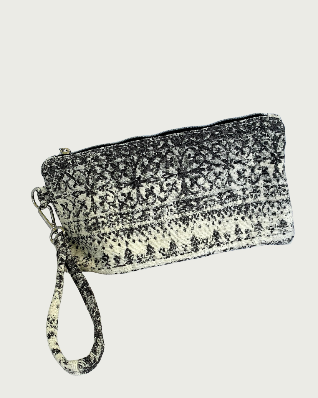 A wristlet in a gray and ivory fair isle-like print with a top zipper closure, gunmetal hardware, and and detachable wrist strap.
